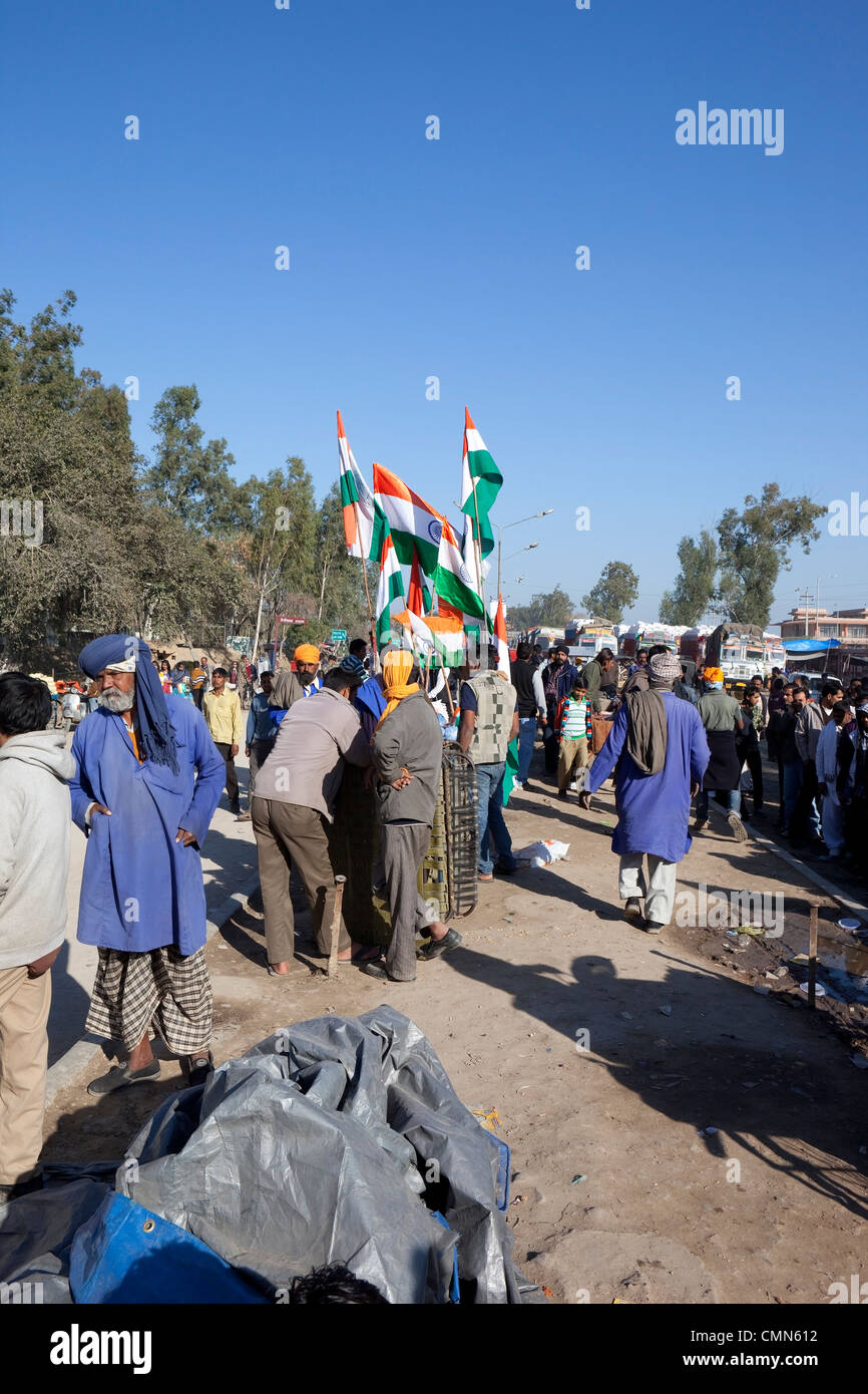 ein Punjabi Flagge Verkäufer an der Wagah Grenze mit indischen Fahnen Menschen LKW und Bäume unter blauem Himmel Stockfoto