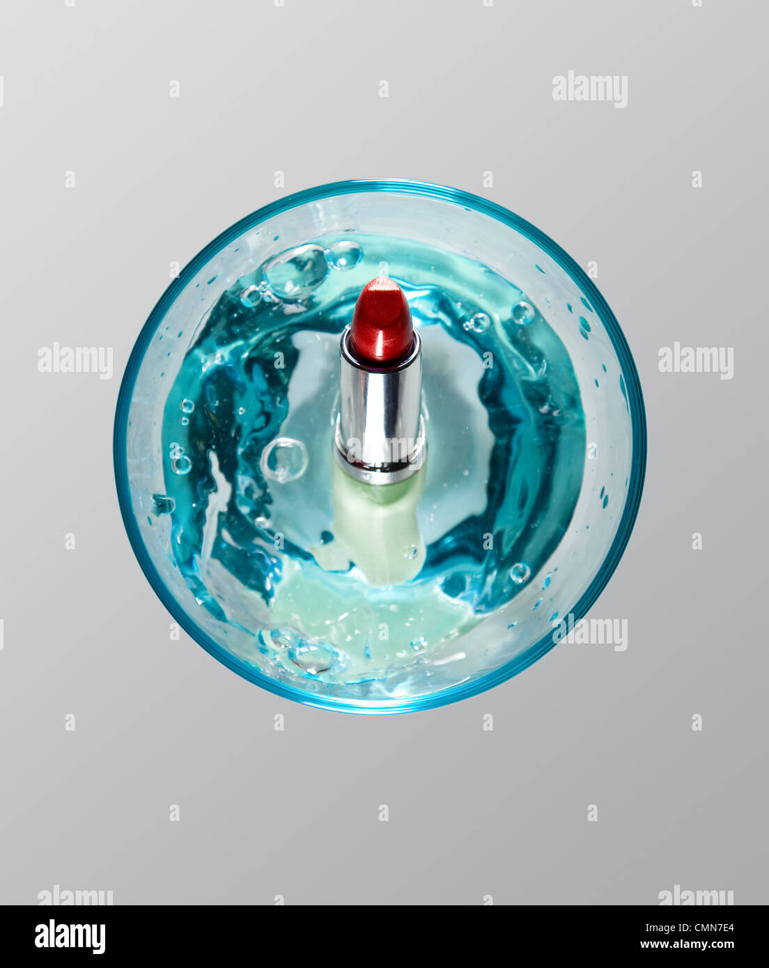 Roter Lippenstift in blauem Glas mit Splash Stockfoto