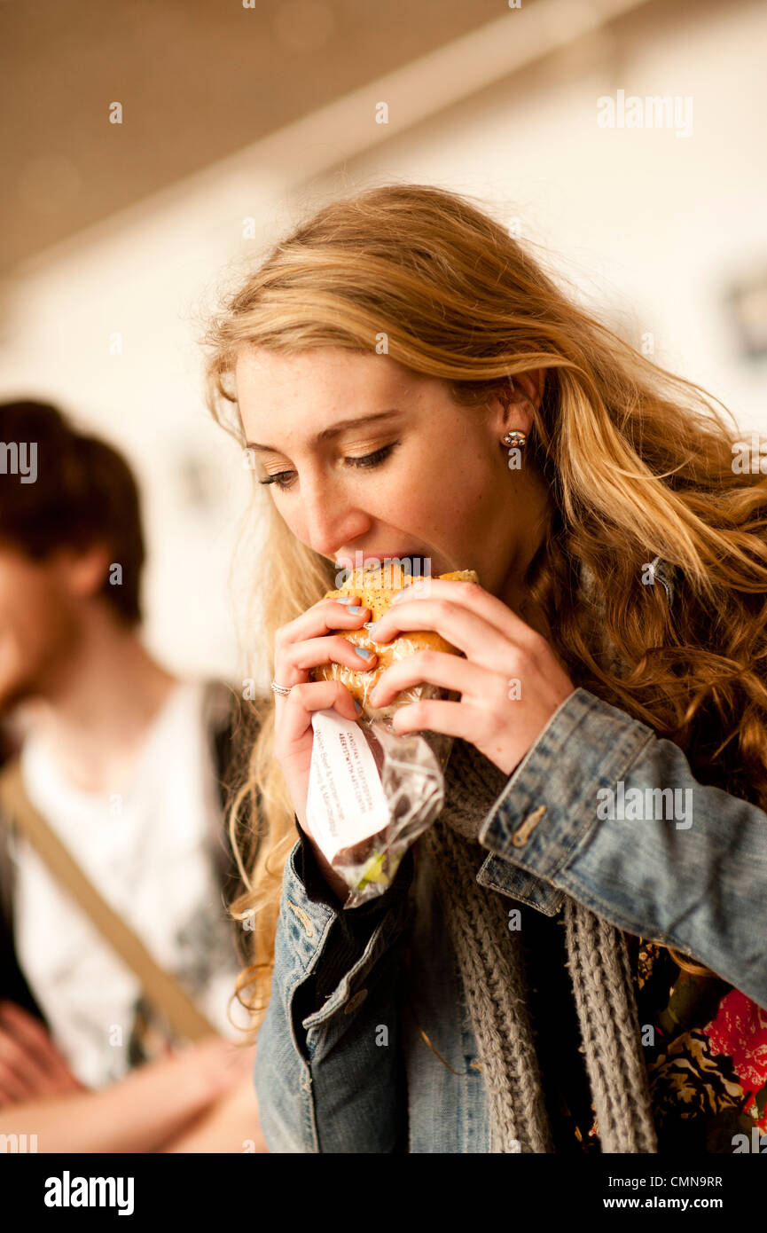 eine junge blonde Frau ein gesundes Brot essen roll Sandwich Essen in einem Universität Mensa Mensa Café, UK Stockfoto