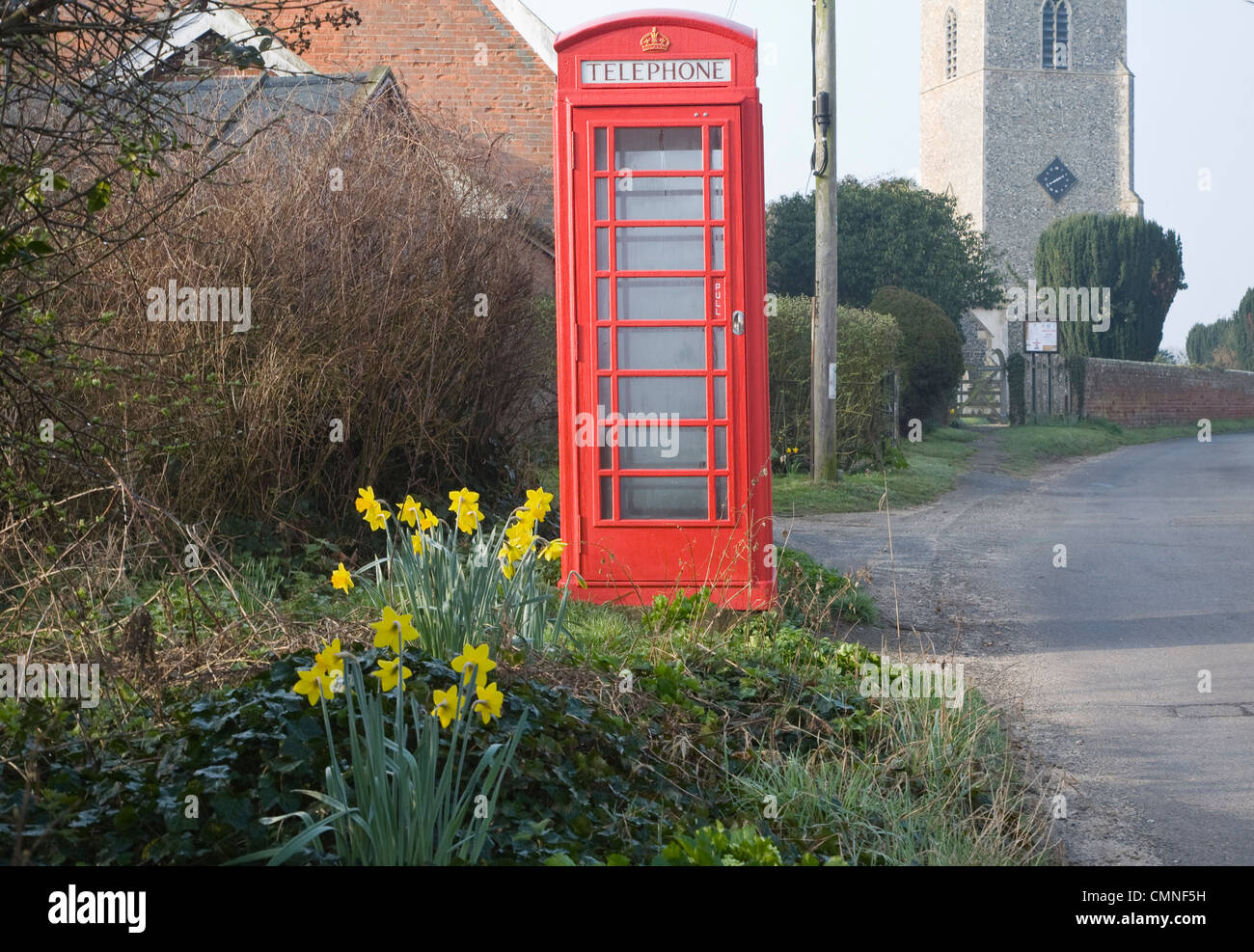 Rote traditionelle Telefon Box Narzissen Dorfstraße mit Kirche, große Glemham, Suffolk, England Stockfoto