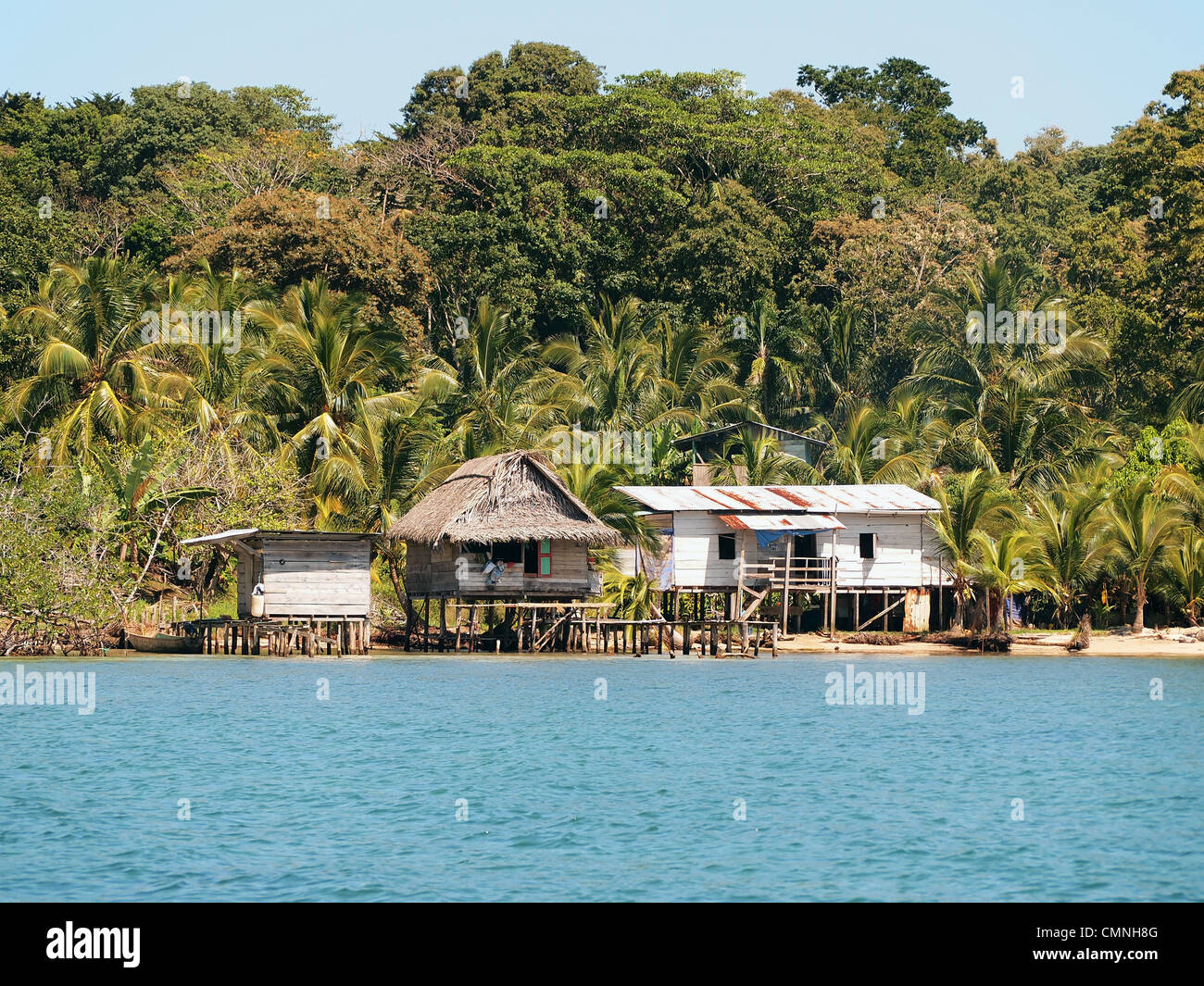 Rustikale Häuser auf Stelzen über dem Meer mit üppiger tropischer Vegetation im Hintergrund, Bocas del Toro, Panama, Mittelamerika Stockfoto