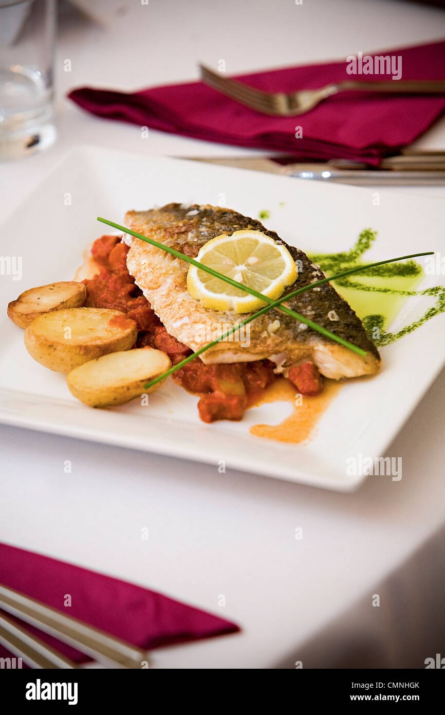 Gebackener Fisch serviert auf quadratischen Platte mit Bratkartoffeln, Scheibe Zitrone und Zitronengras. Stockfoto