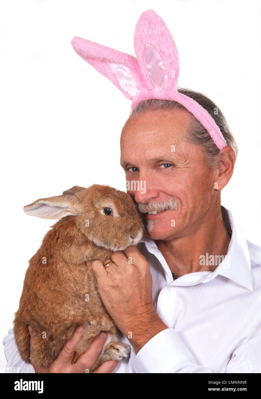 Lächelnder Mann trägt Hasenohren und hält ein Kaninchen. Stockfoto