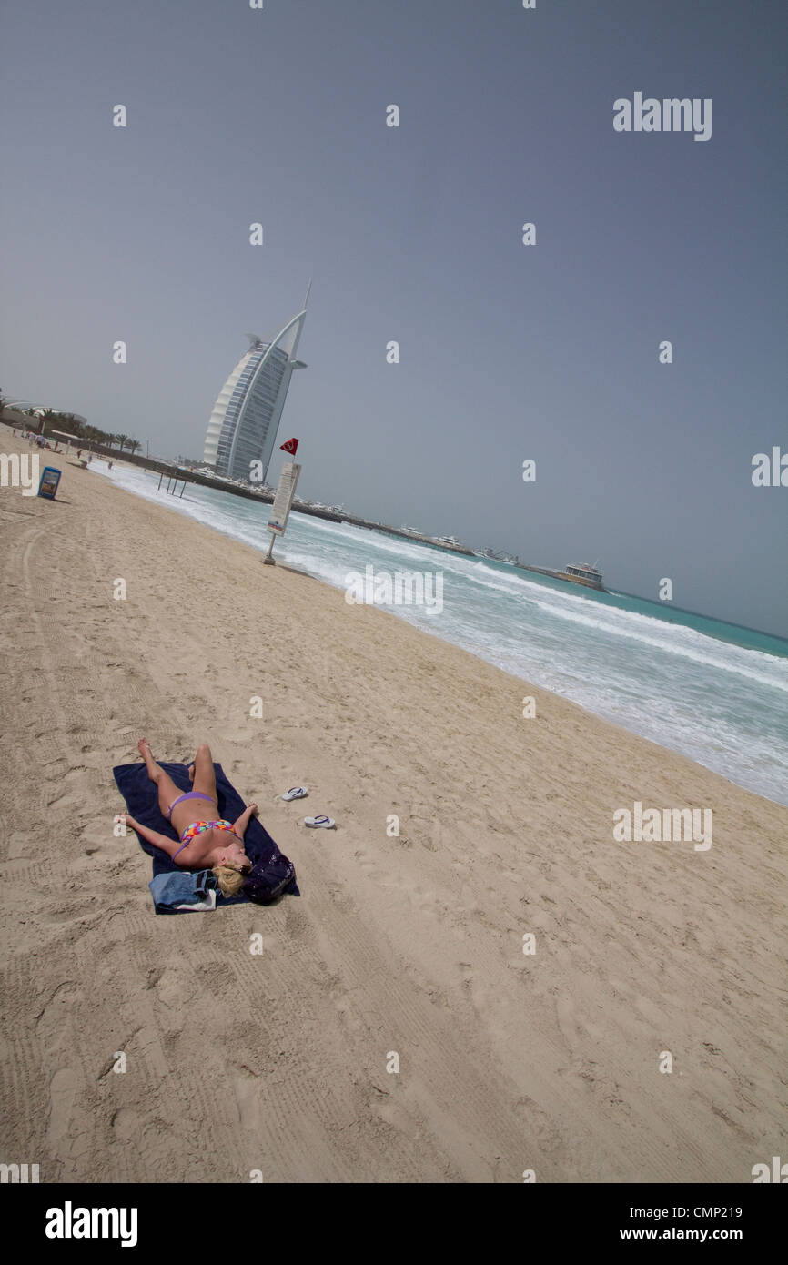 Vereinigte Arabische Emirate, Dubai – Ein Tourist entspannt und sonnt sich am leeren Strand mit dem berühmten Burj Al Arab, dem Turm der Araber, der majestätisch im Hintergrund aufsteigt und Luxus und Freizeit im Herzen von Dubai symbolisiert. Stockfoto