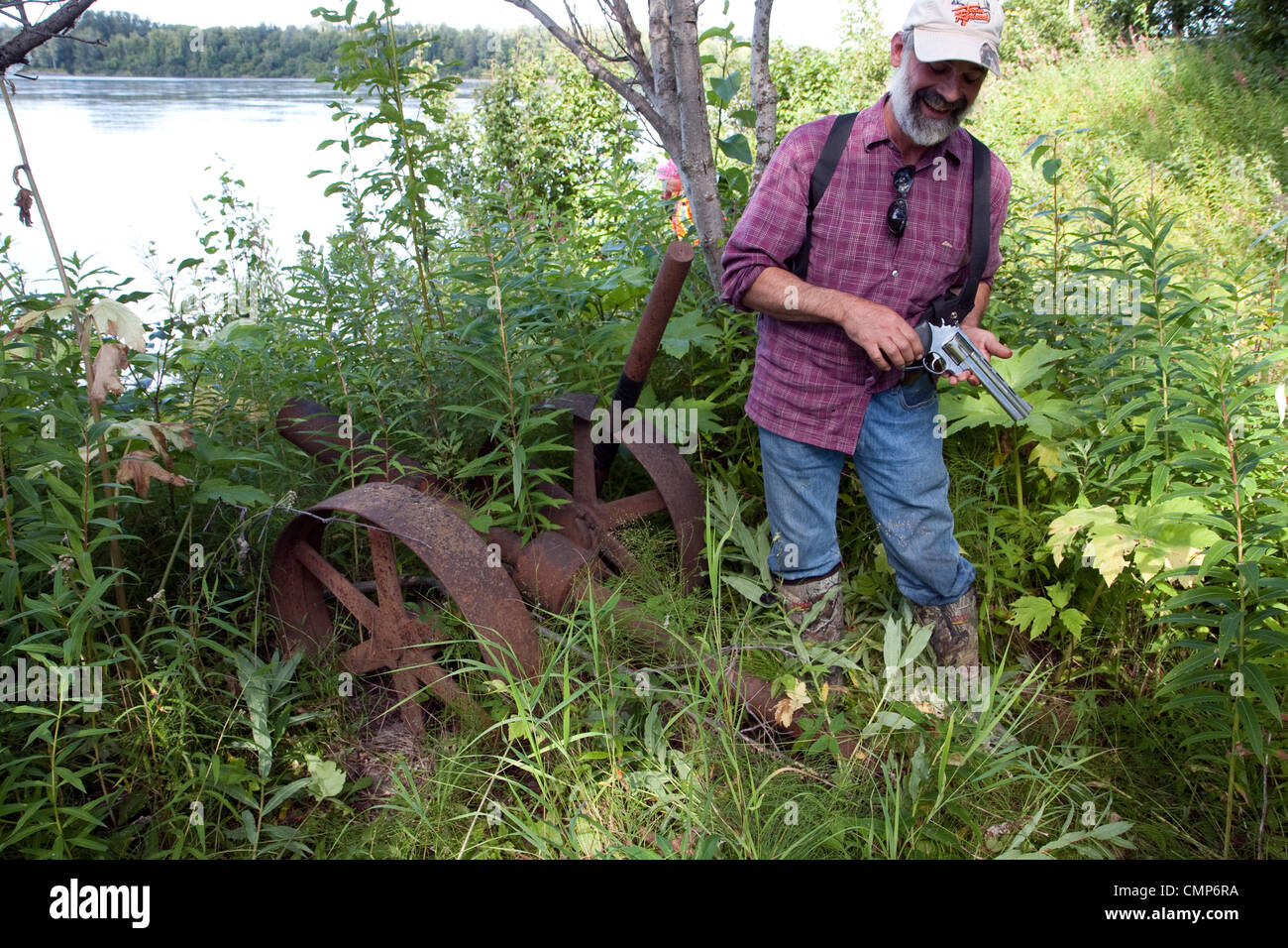 Ein Mann zeigt seine Bären Waffe beim stehen in der Nähe einige rostige Räder in der historischen Stadt Website Susitna, Alaska, USA Stockfoto