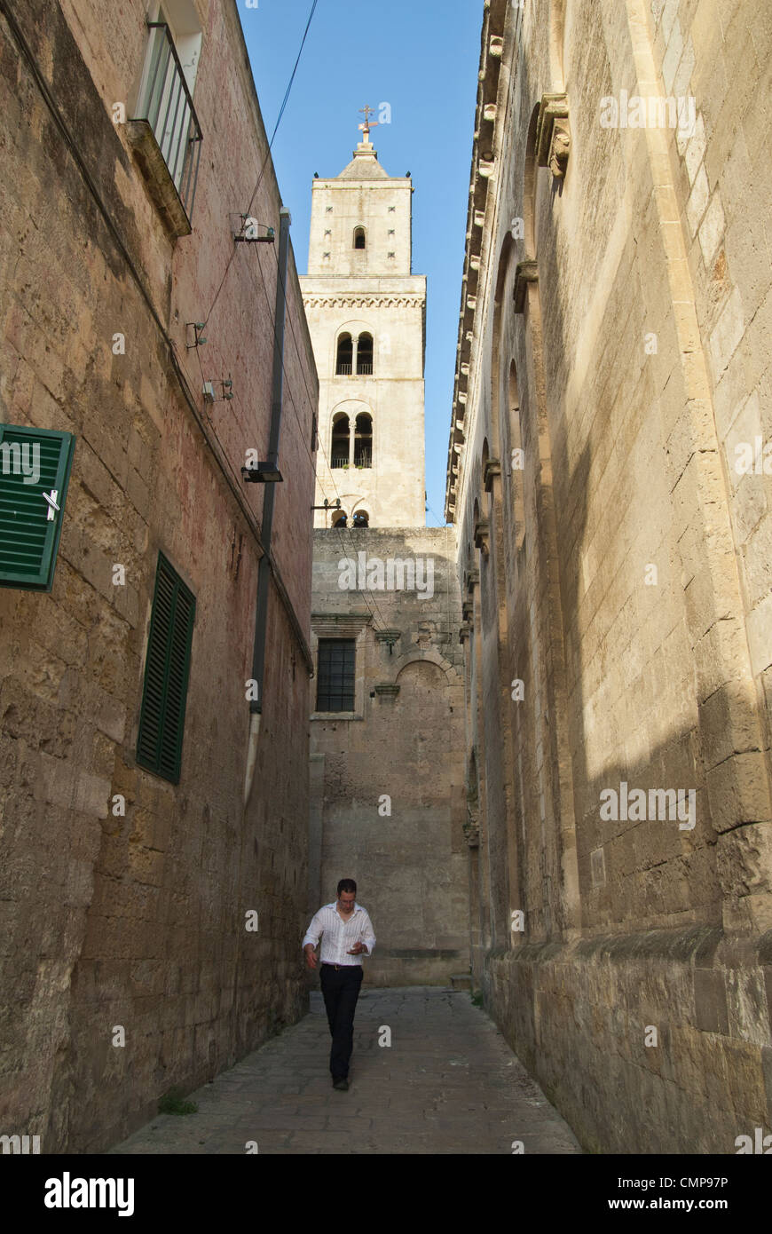 Ein italienischer Mann geht durch eine schmale Gasse, überragt von der Bell Turm der Kathedrale von Matera, Italien Stockfoto