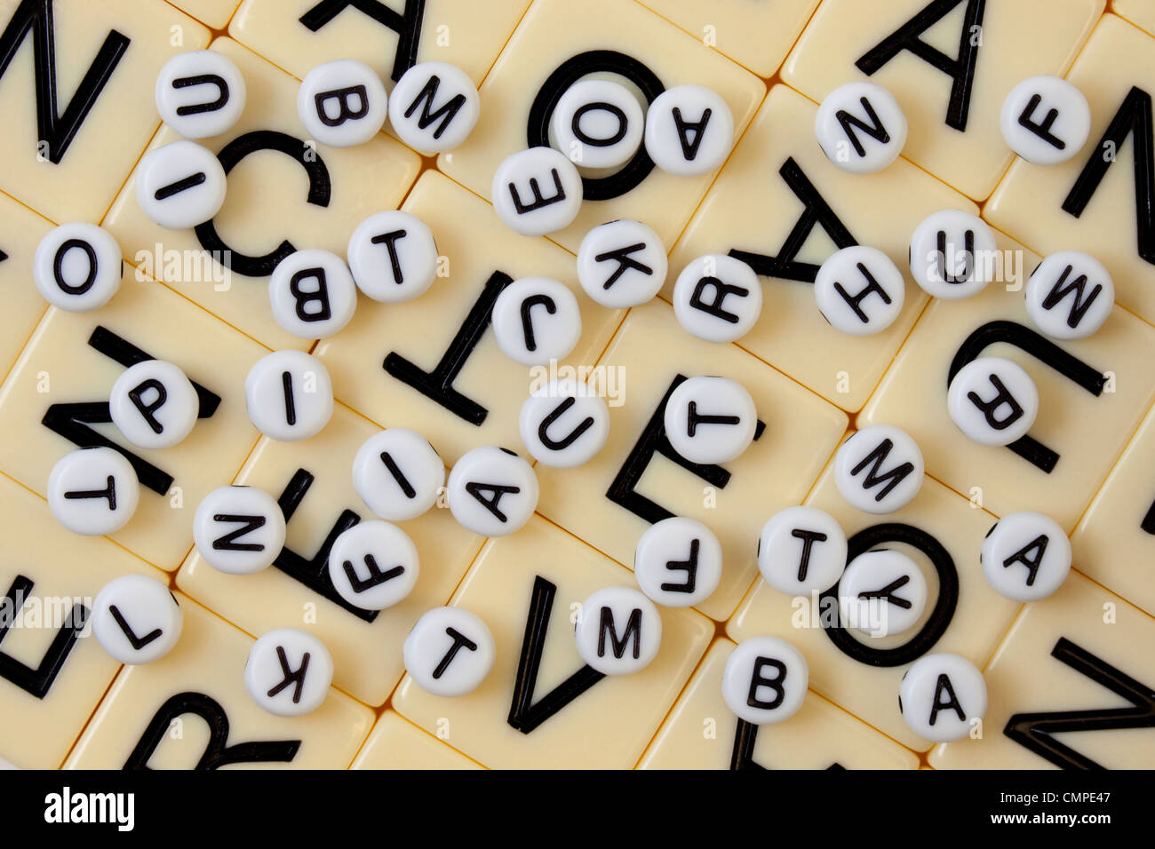 weiße Perlen mit schwarzen Buchstaben auf einem Elfenbein Mosaik mit größeren Buchstaben nach dem Zufallsprinzip verschüttet Stockfoto