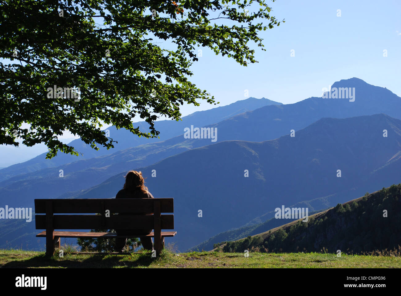 Einsame Frau sitzen auf einer Bank vor Bergen Panorama, Alpen, Piemont, Italien Stockfoto