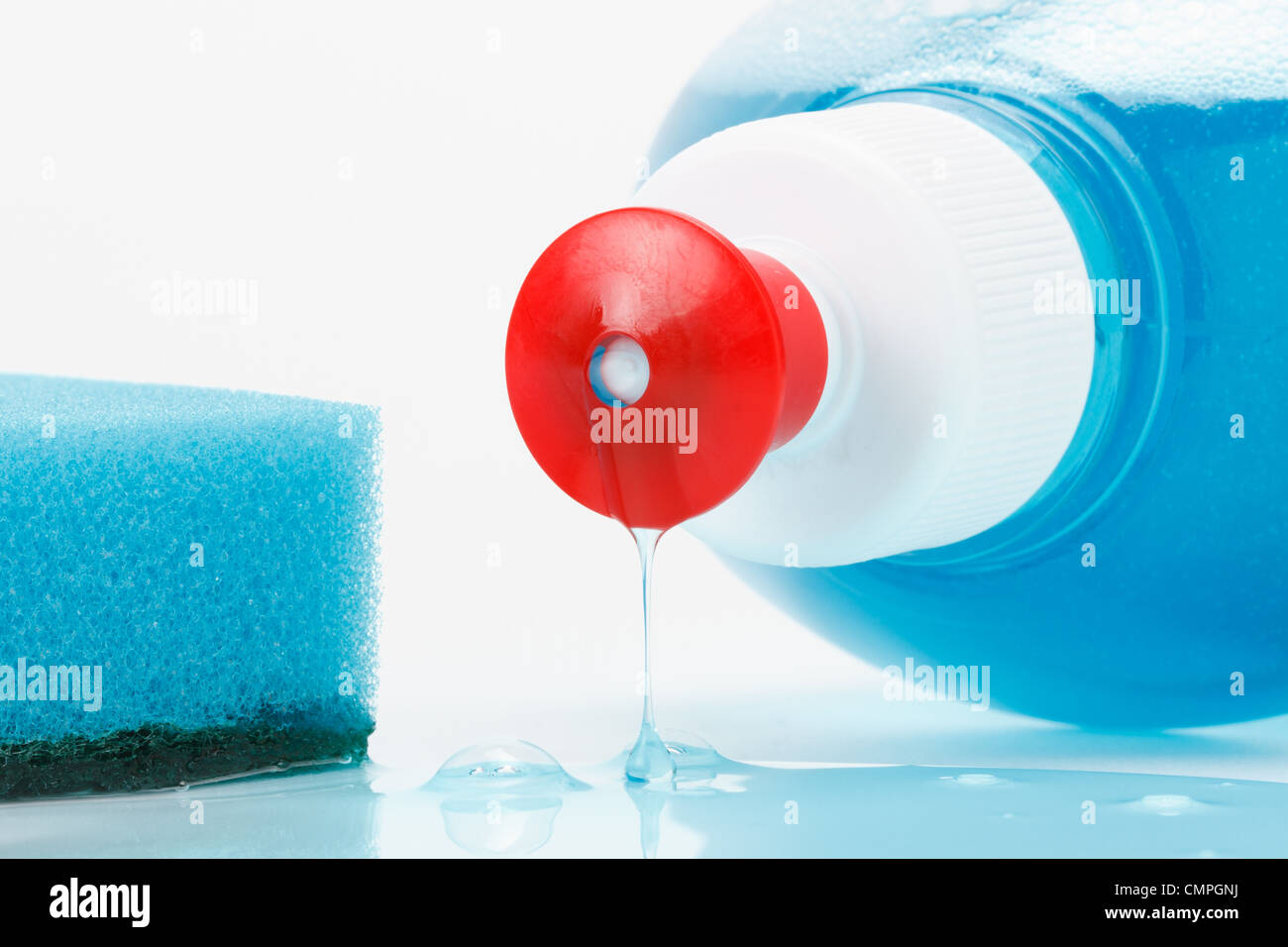 Spülmittel fließt aus der Flasche, blauer Schwamm auf weiß Stockfoto