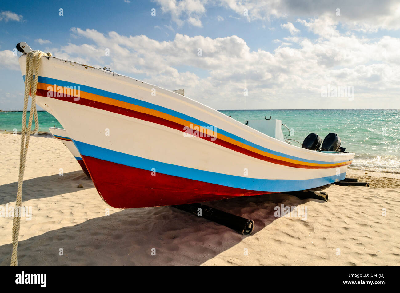 Eine bunt bemalte Boot hochgezogen am Sandstrand in Playa del Carmen auf der mexikanischen Halbinsel Yucatan mit teilweise bewölkter Himmel im Hintergrund. Stockfoto