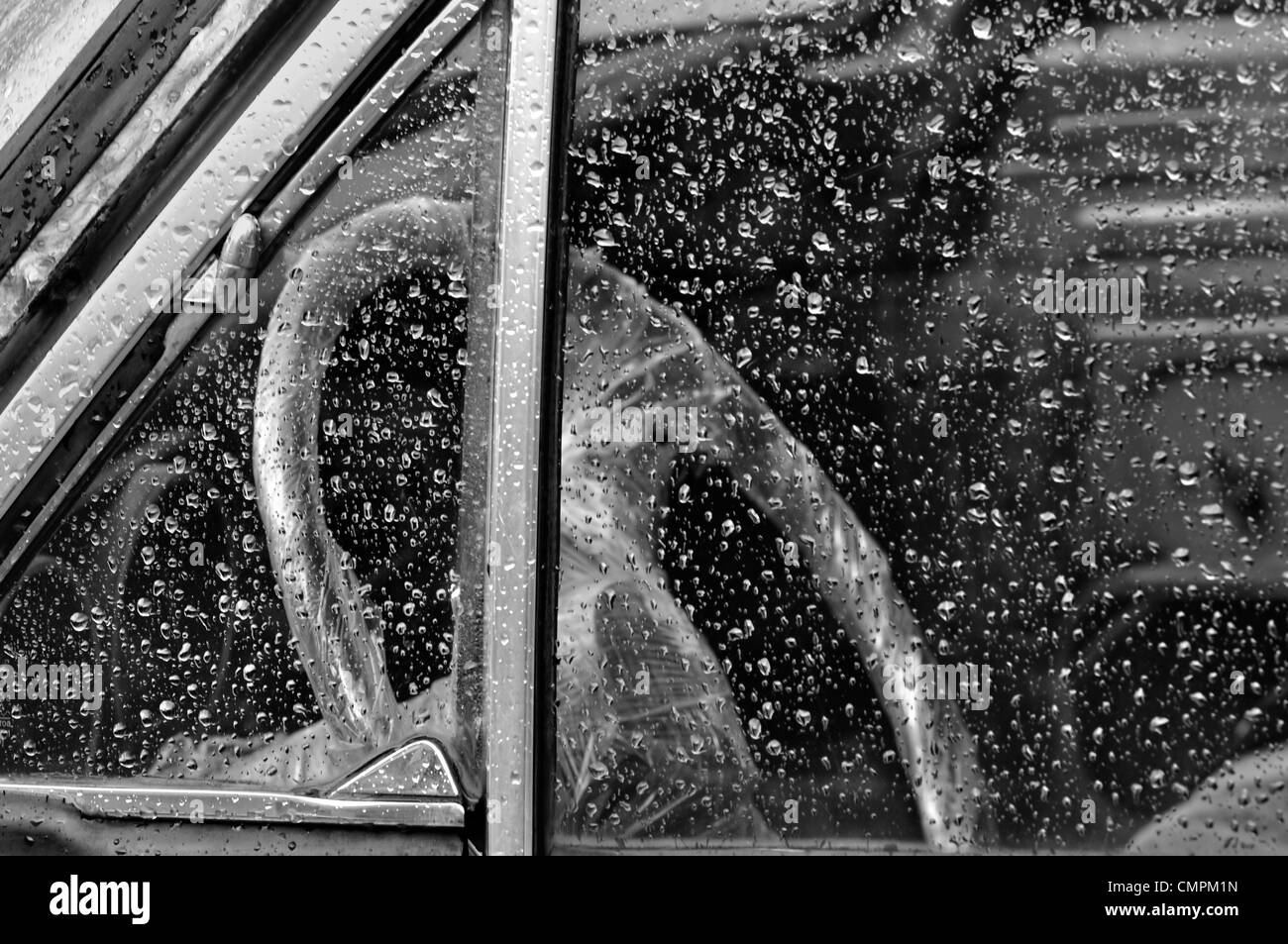 Oldtimer-Innenraum durch Regen überdachte Fenster Lenkrad in Plastik verpackt. Schwarz und weiß. Stockfoto