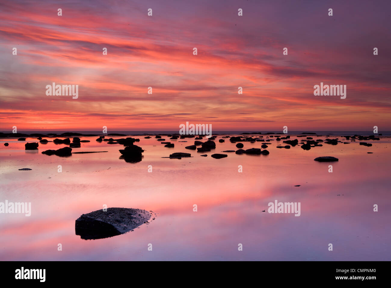 Felsbrocken und Reflexionen im Meer bei Sonnenaufgang, gegen Bay, Yorkshire, England, Vereinigtes Königreich, Europa Stockfoto