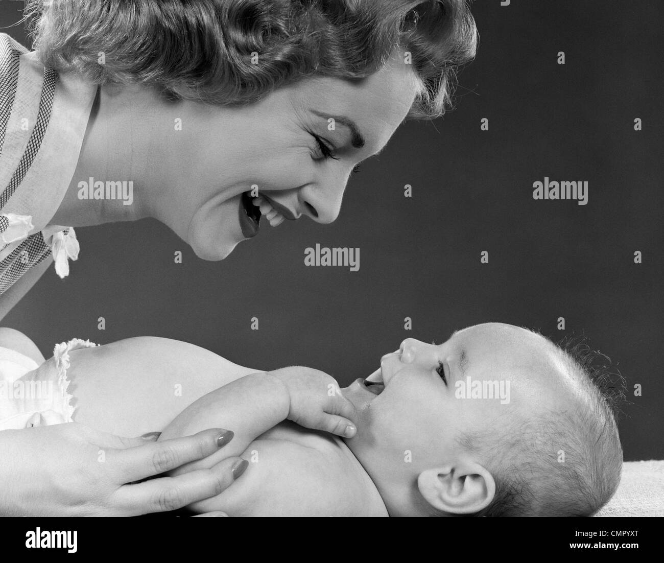 1950ER JAHREN NAHAUFNAHME PROFIL VON LÄCHELNDEN MUTTER BEUGTE SICH ZU LACHEN BABY AUF BETT LIEGEND Stockfoto