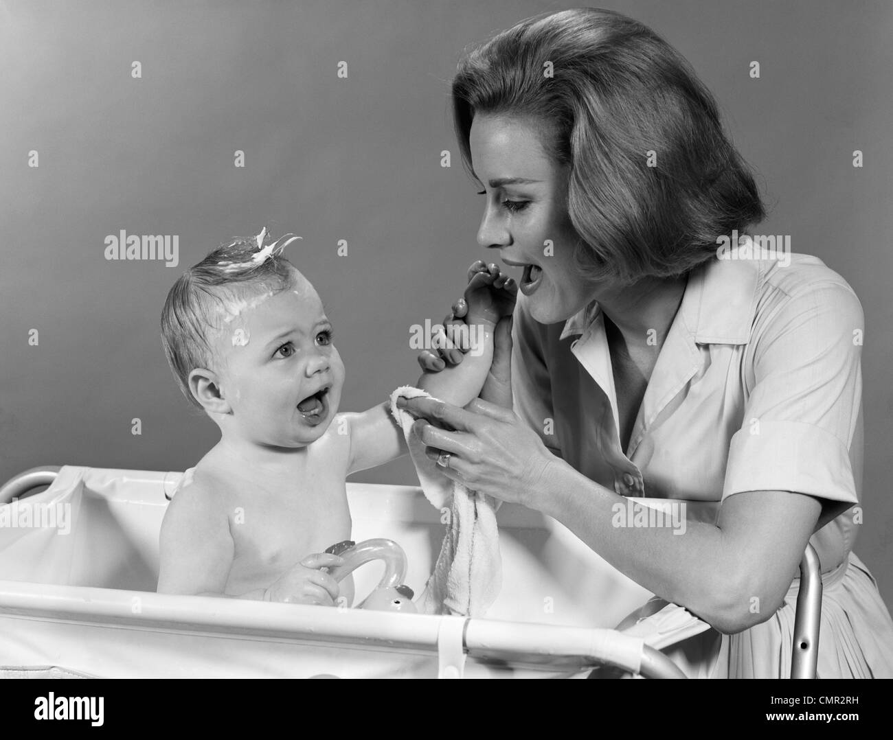 1960ER JAHREN MUTTER WASCHEN BABY IM BABY-BADEWANNE Stockfoto