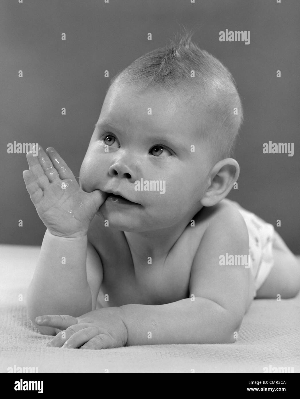 1950ER JAHRE PORTRAIT BABY LIEGEND AUF BAUCH MIT DAUMEN IM MUND Stockfoto