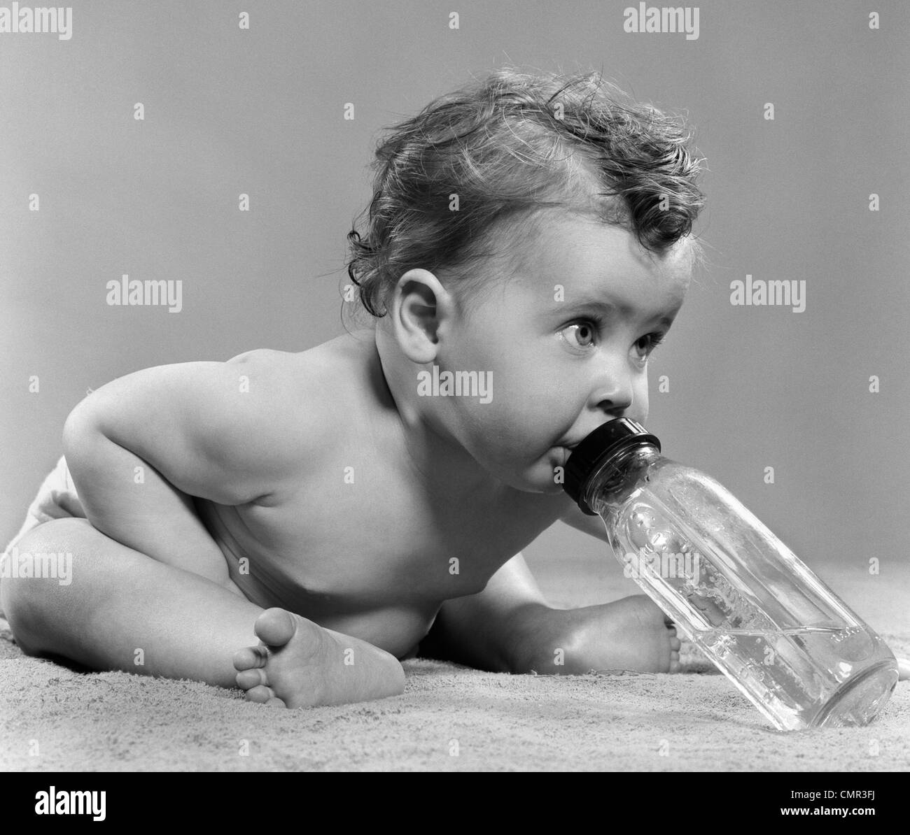 1950ER JAHRE BABY SITTING LEHNT SICH NACH VORNE TRINKEN AUS DER FLASCHE STUDIO INDOOR Stockfoto
