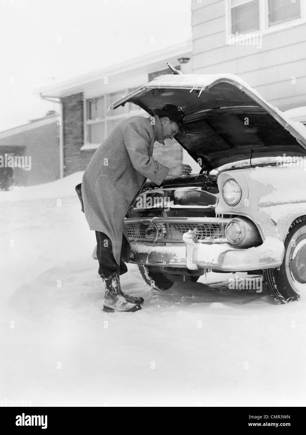 1950ER JAHRE MANN WINTER AUFFAHRT FIX MOTORHAUBE STARTEN WOLLEN Stockfoto