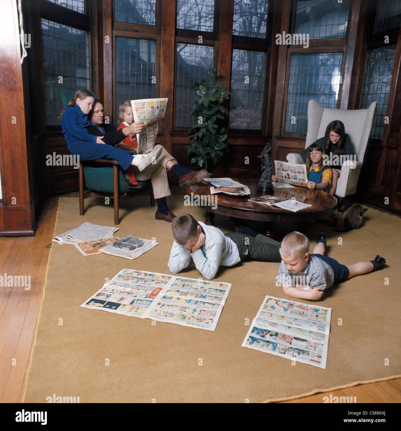 1970ER JAHRE FAMILIE 7 LESUNG SONNTAGSZEITUNGEN UND COMICS IM WOHNZIMMER Stockfoto