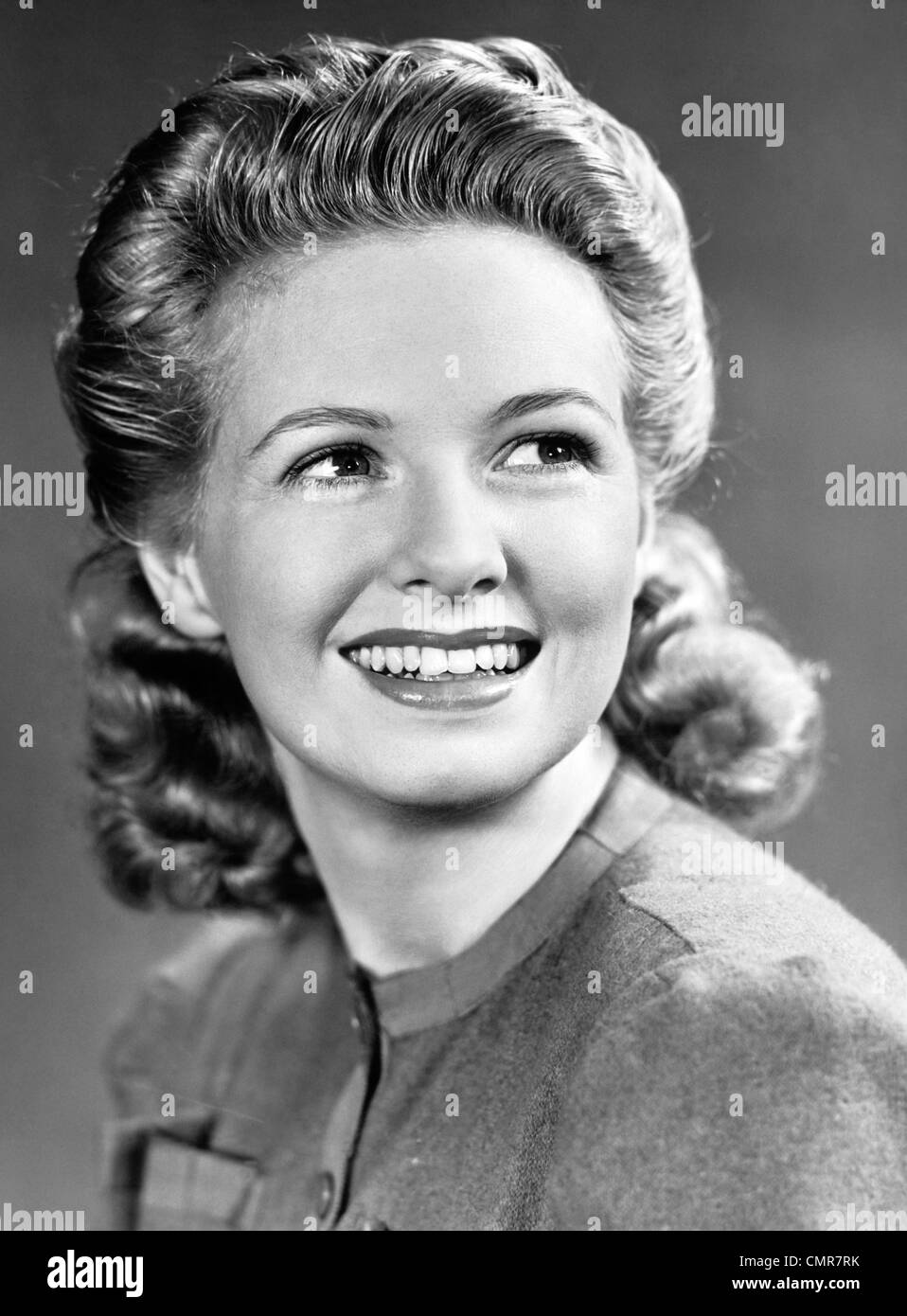 1940ER JAHRE PORTRAIT DER LÄCHELNDE FRAU MIT LANGEN BLONDEN LOCKIGEN HAAREN Stockfoto