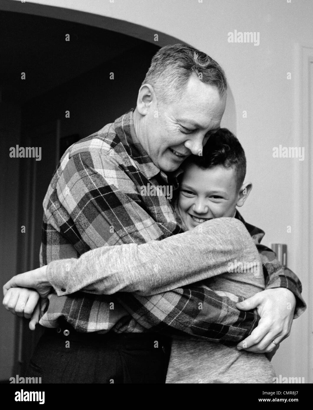 1950S 1960S LÄCHELN VATER UND SOHN UMARMT INDOOR Stockfoto