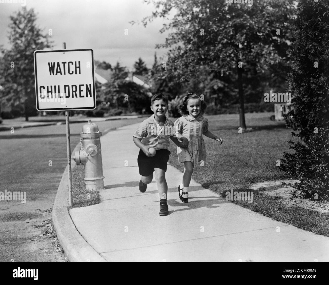 1950ER JAHREN KINDER ZU FUß AUF DEM BÜRGERSTEIG UHR KINDER ZEICHEN ÜBERSPRINGEN Stockfoto