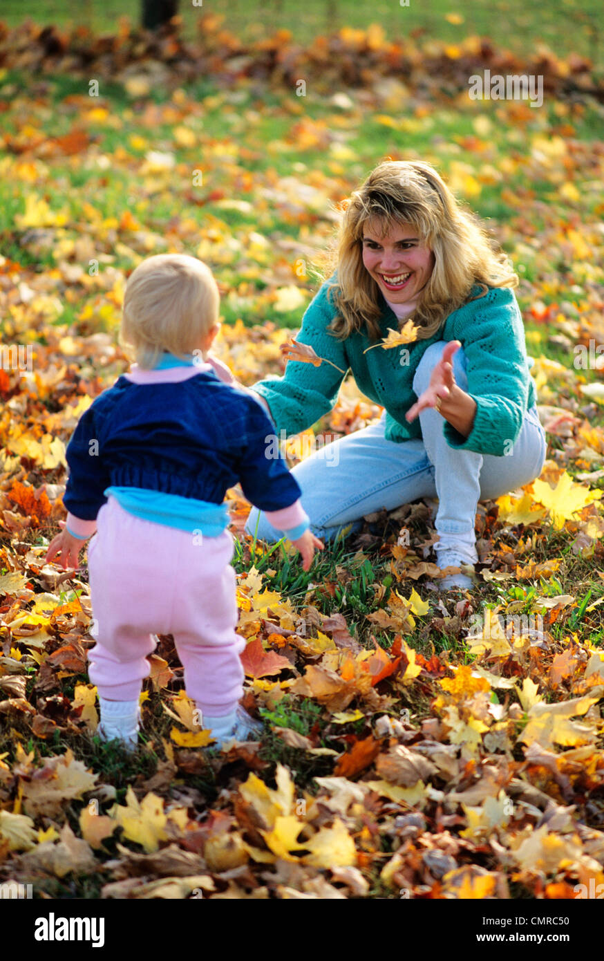 1990ER JAHREN MUTTER UND KLEINKIND SPIELEN IM HERBSTLAUB Stockfoto