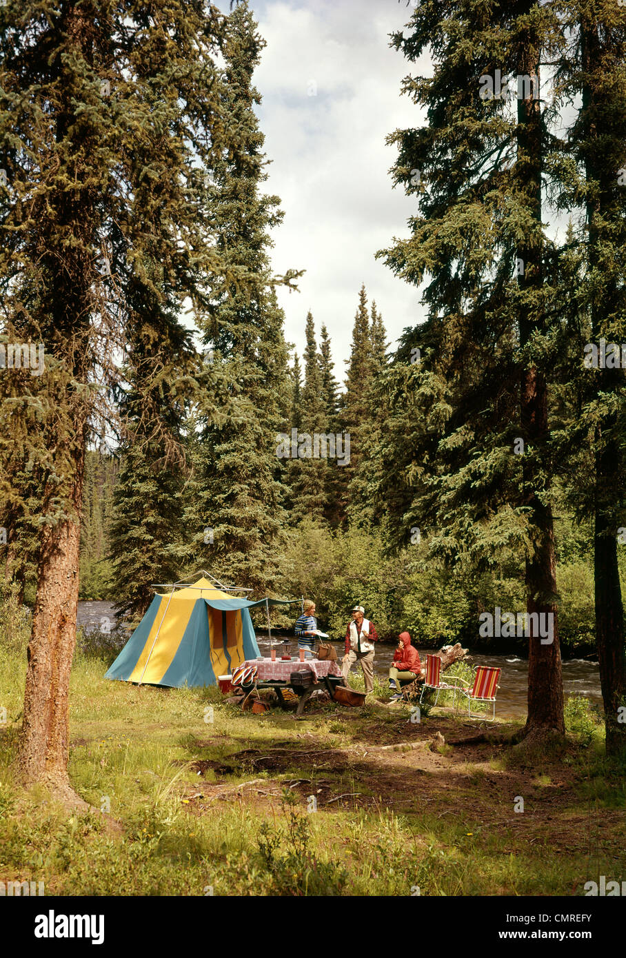 1970S 1980S FAMILIE CAMPING IM PINIENWALD NEBEN BACH Stockfoto