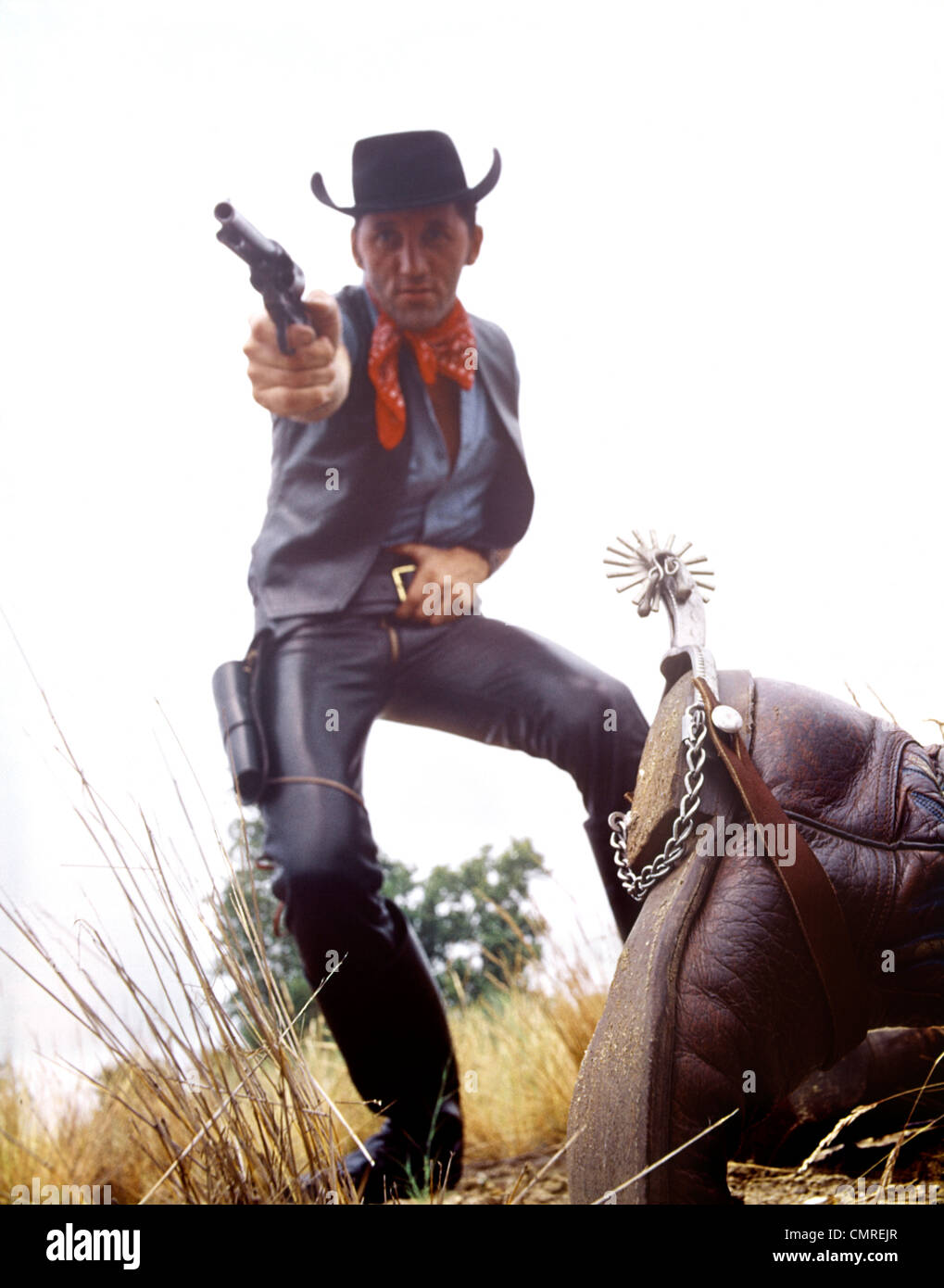 1960ER JAHRE MANN COWBOY IM SCHWARZEN HUT SCHIEßEN PISTOLE TOTEN MANN AM BODEN Stockfoto
