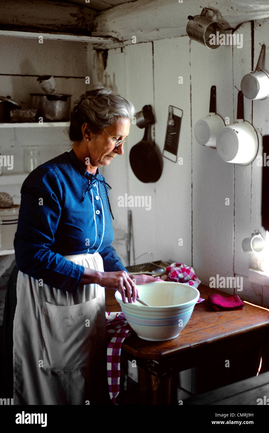 1970ER JAHRE ÄLTERE FRAU BEREITET ESSEN IN LÄNDLICHEN FRONTIER KÜCHE Stockfoto