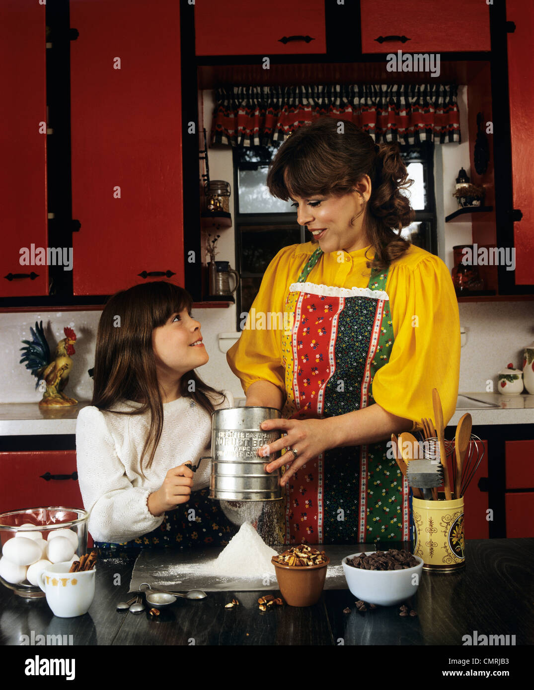 1980ER JAHRE MUTTER UND TOCHTER BACKEN SICHTEN MEHL IN KÜCHE Stockfoto