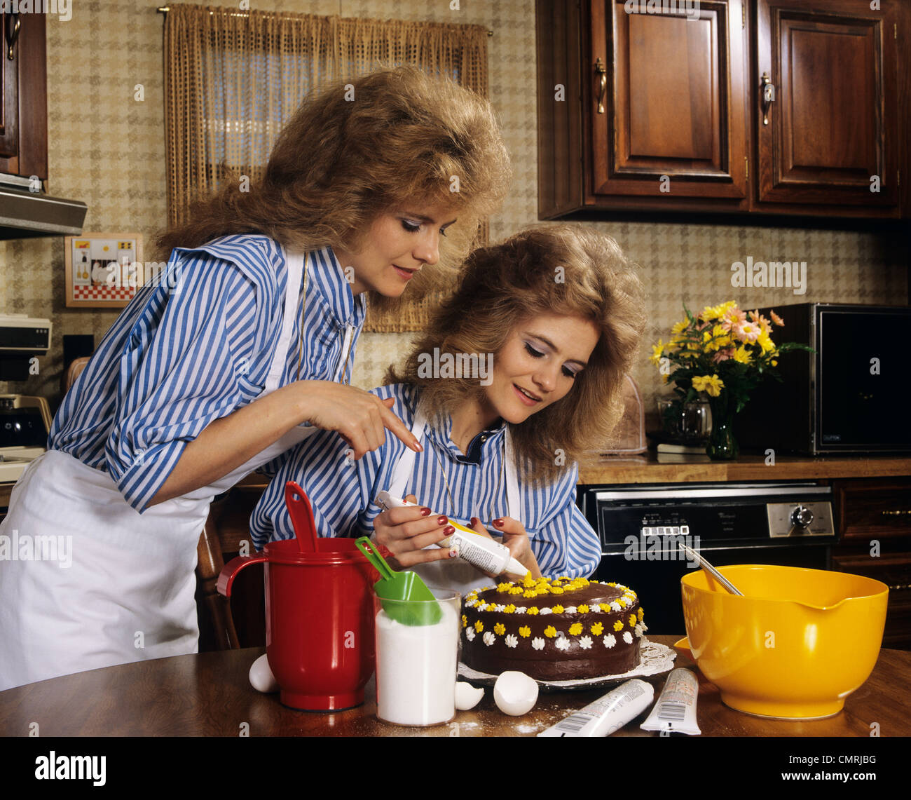 1970ER JAHRE MUTTER TOCHTER GEKLEIDET GLEICHERMAßEN DEKORIEREN KUCHEN Stockfoto