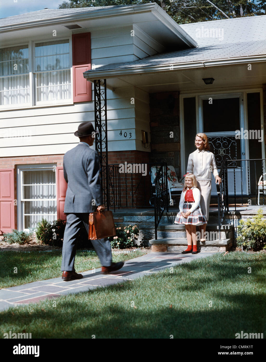 1950ER JAHRE MUTTER TOCHTER WARTEN SCHRITTE HAUS FÜR VATER AKTENTASCHE COMING HOME S FAMILIE MANN FRAU MÄDCHEN RETRO Stockfoto