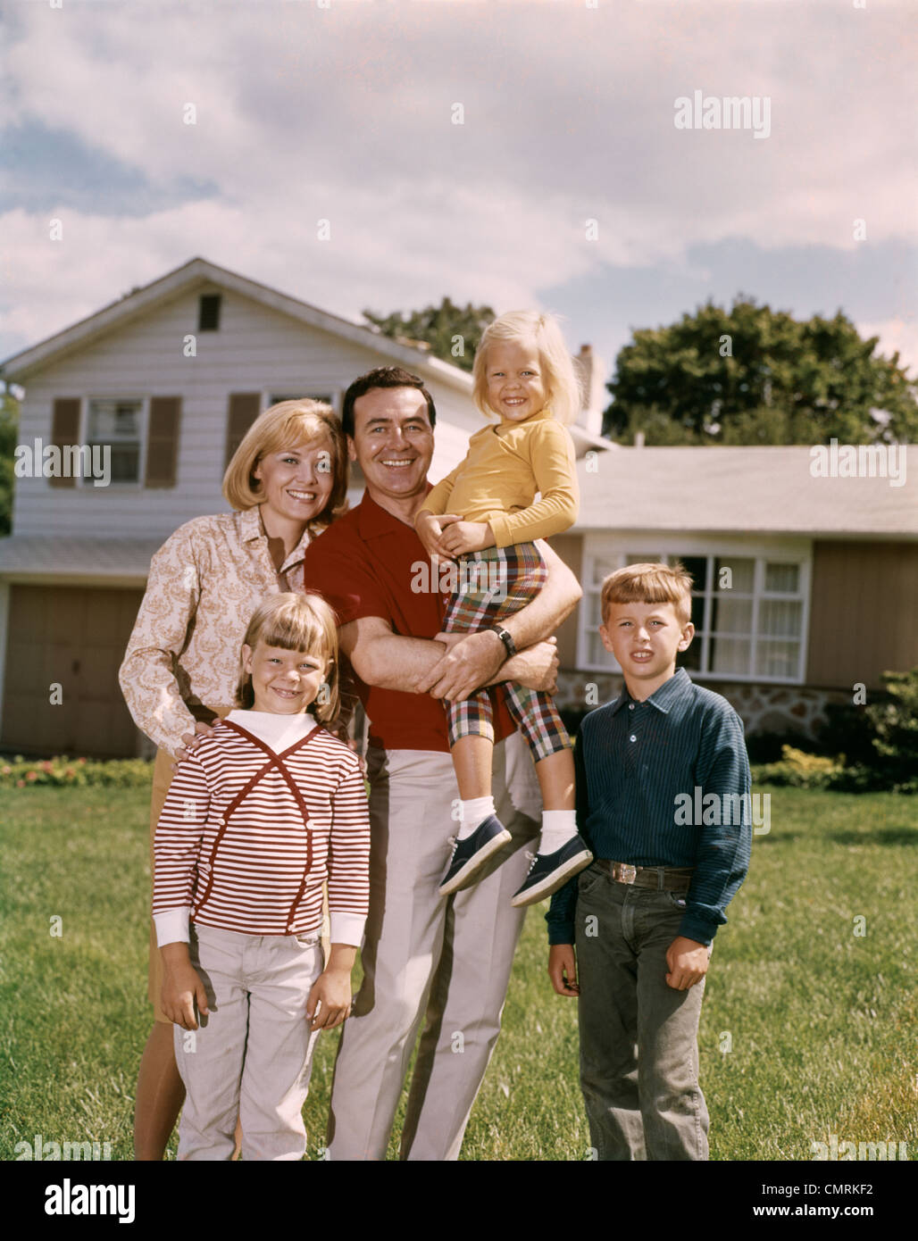 1960ER JAHREN FAMILIENPORTRÄT STEHT MAN VOR EINEN S SPLIT LEVEL HAUS VATER MUTTER 2 TÖCHTER SOHN LÄCHELND Stockfoto