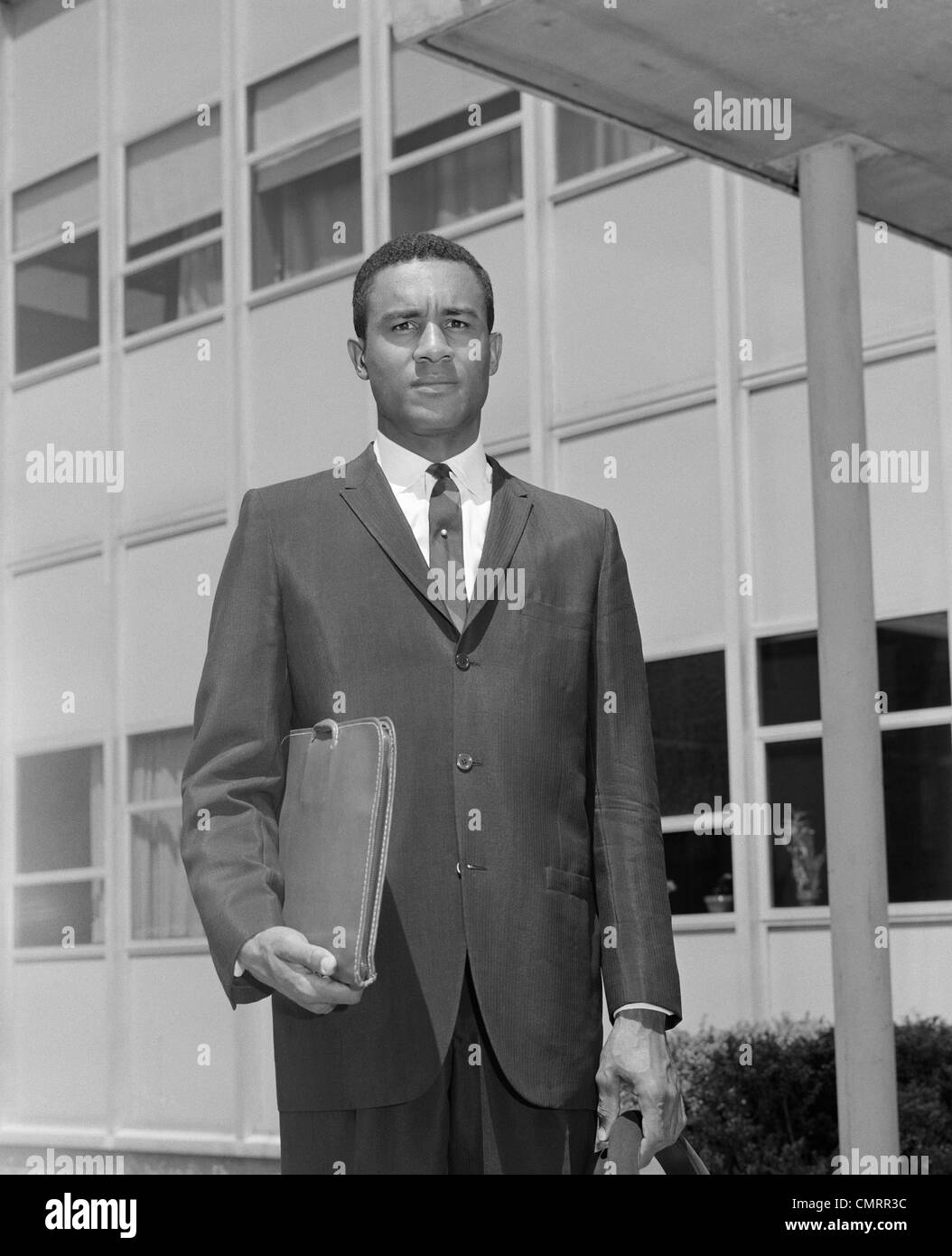 1960ER JAHRE AFRIKANISCH-AMERIKANISCHER GESCHÄFTSMANN HOLDING AKTENTASCHE IM FREIEN Stockfoto
