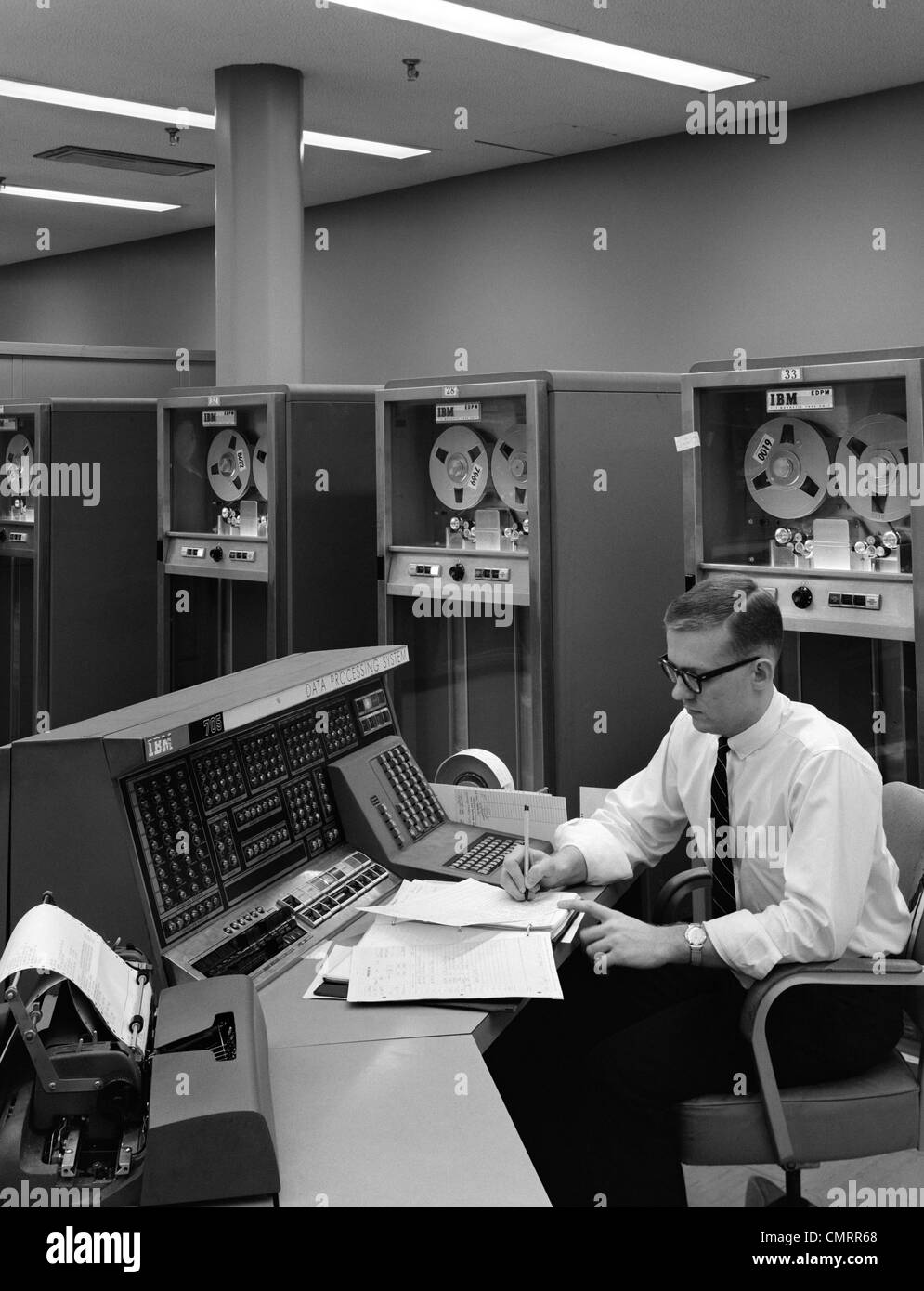 1960ER JAHRE MANN IM HEMD & TIE & GLÄSER AM LEITSTAND FÜR IBM DATENVERARBEITUNGSSYSTEM Stockfoto