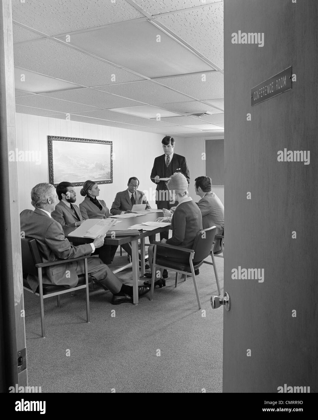 1970ER JAHRE GRUPPE 7 EXECUTIVE BUSINESS LEUTE KONFERENZTISCH ANGESEHEN DURCH OFFENE TÜR Stockfoto