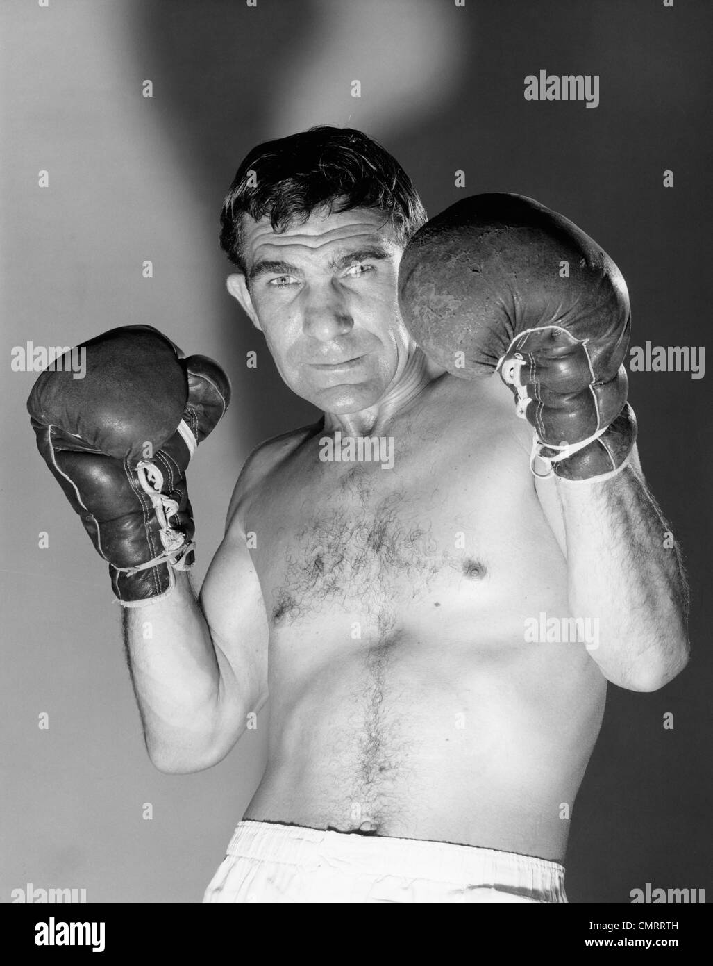 1960ER JAHRE PORTRAIT DER BOXER HÄLT BEHANDSCHUHTEN HÄNDE GESICHT, BLICK IN DIE KAMERA ZU SCHÜTZEN Stockfoto