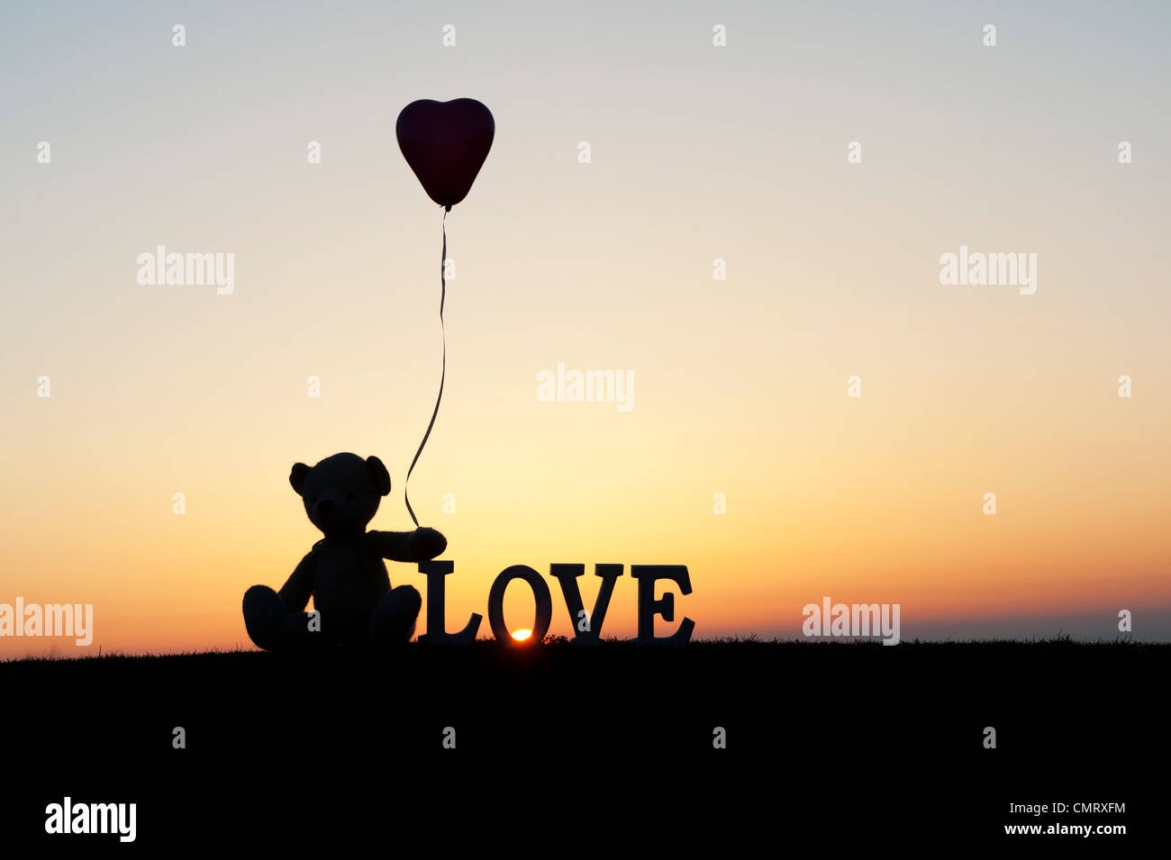 Teddy Bär hält ein Herzballon Form als nächstes auch das Wort Liebe bei Sonnenaufgang Stockfoto