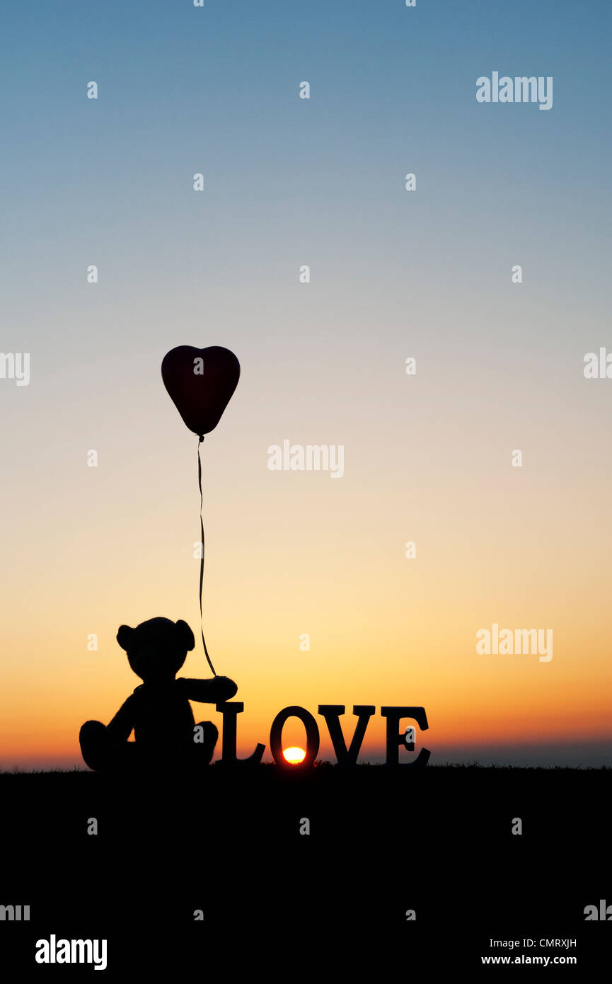 Teddy Bär hält ein Herzballon Form als nächstes auch das Wort Liebe bei Sonnenaufgang Stockfoto