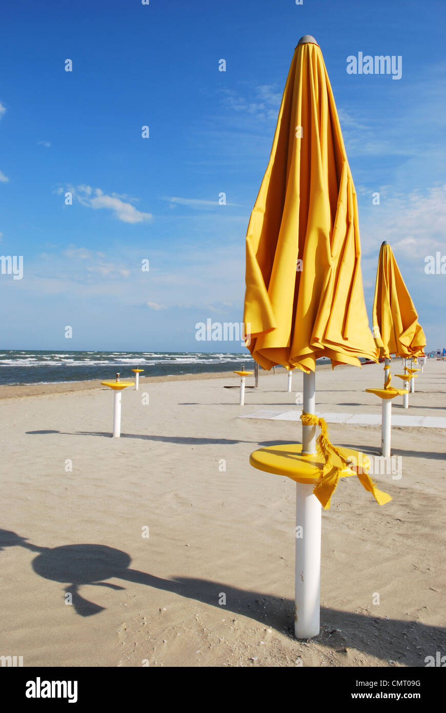 Gelbe geschlossene Sonnenschirme am leeren Strand in einem windigen Sonnentag, Rimini, Italien Stockfoto