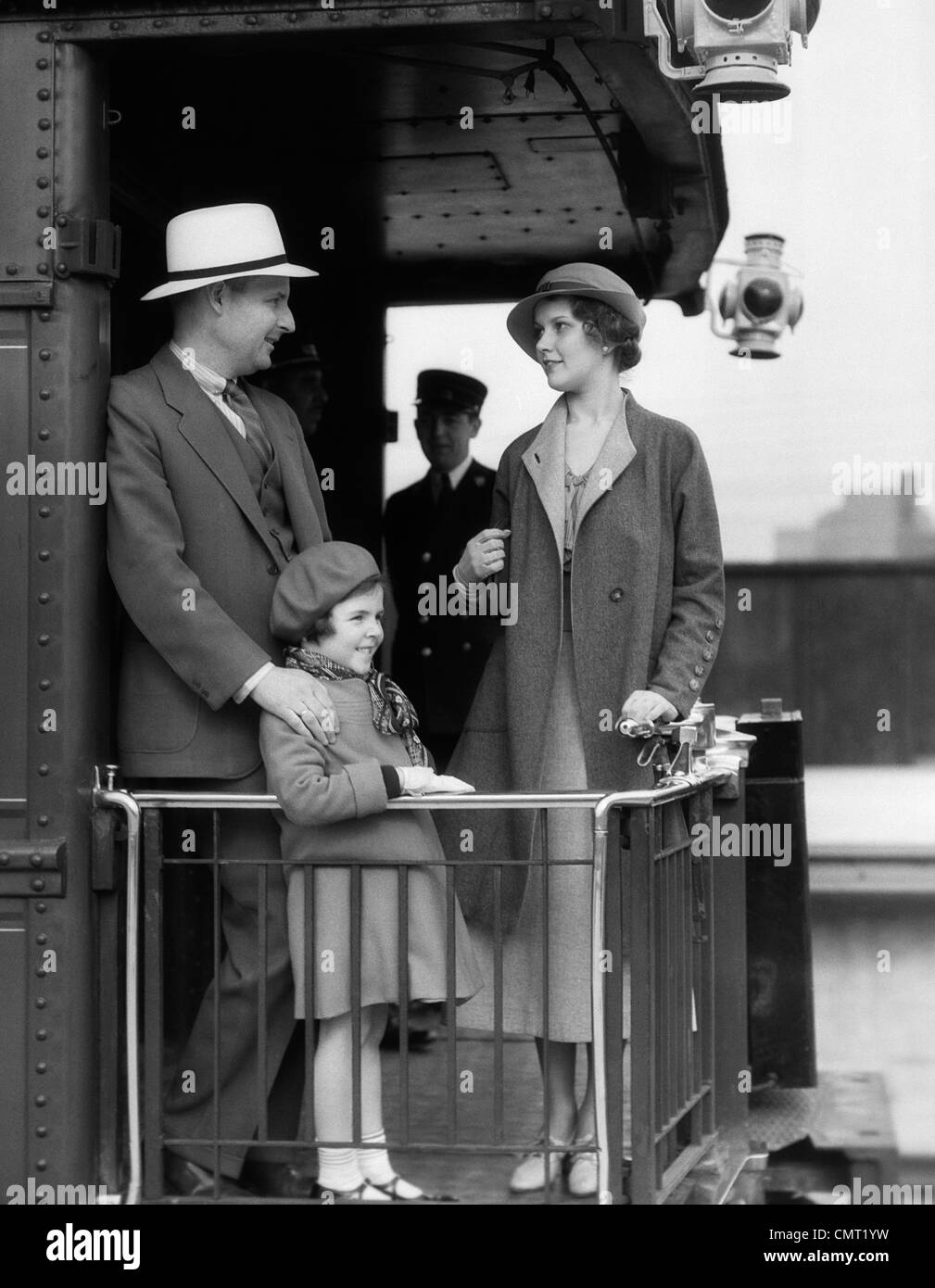 1930ER JAHRE FAMILIE VON DREI AM GELÄNDER AT RÜCKSEITE WAGGON MIT TRÄGERN STEHEN IM HINTERGRUND Stockfoto