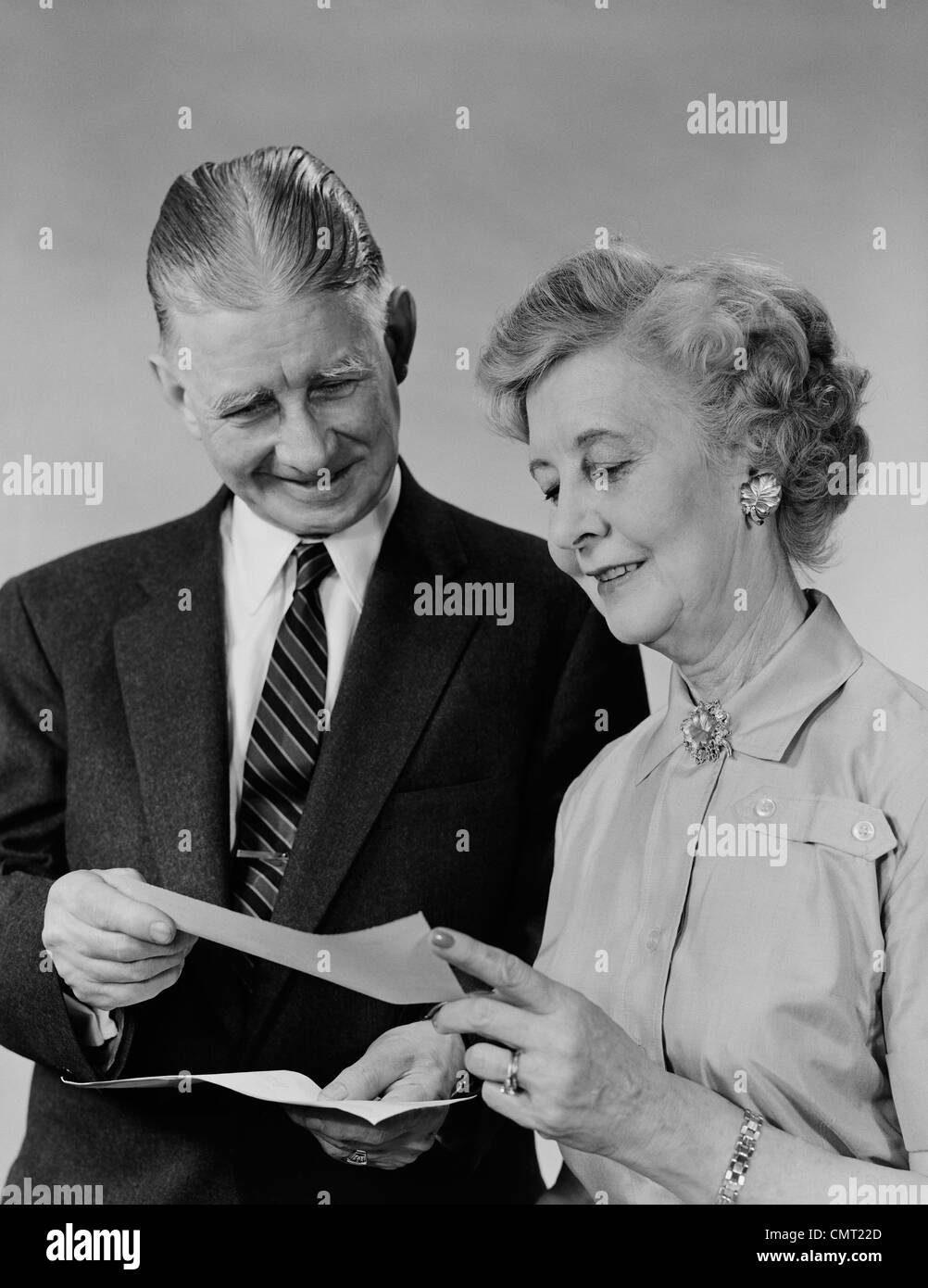 1960ER JAHRE ÄLTERES PAAR MANN FRAU LESUNG HALTEN CHECK Stockfoto