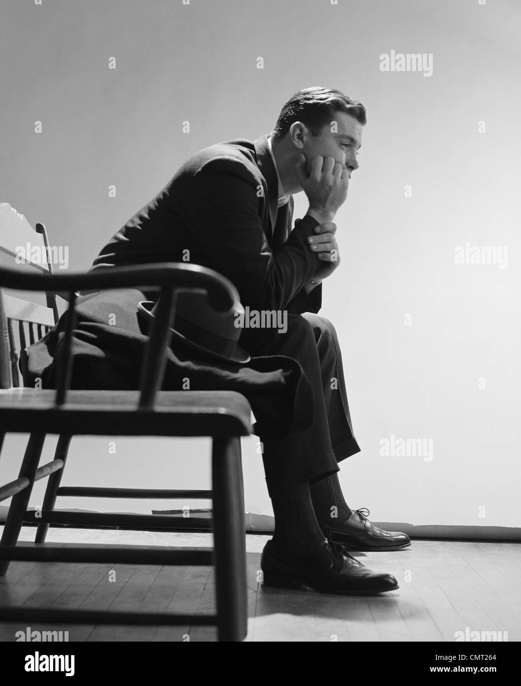 1960ER JAHREN TRAURIGER MANN RUHT HAND AM KINN SITZEN AUF BANK Stockfoto