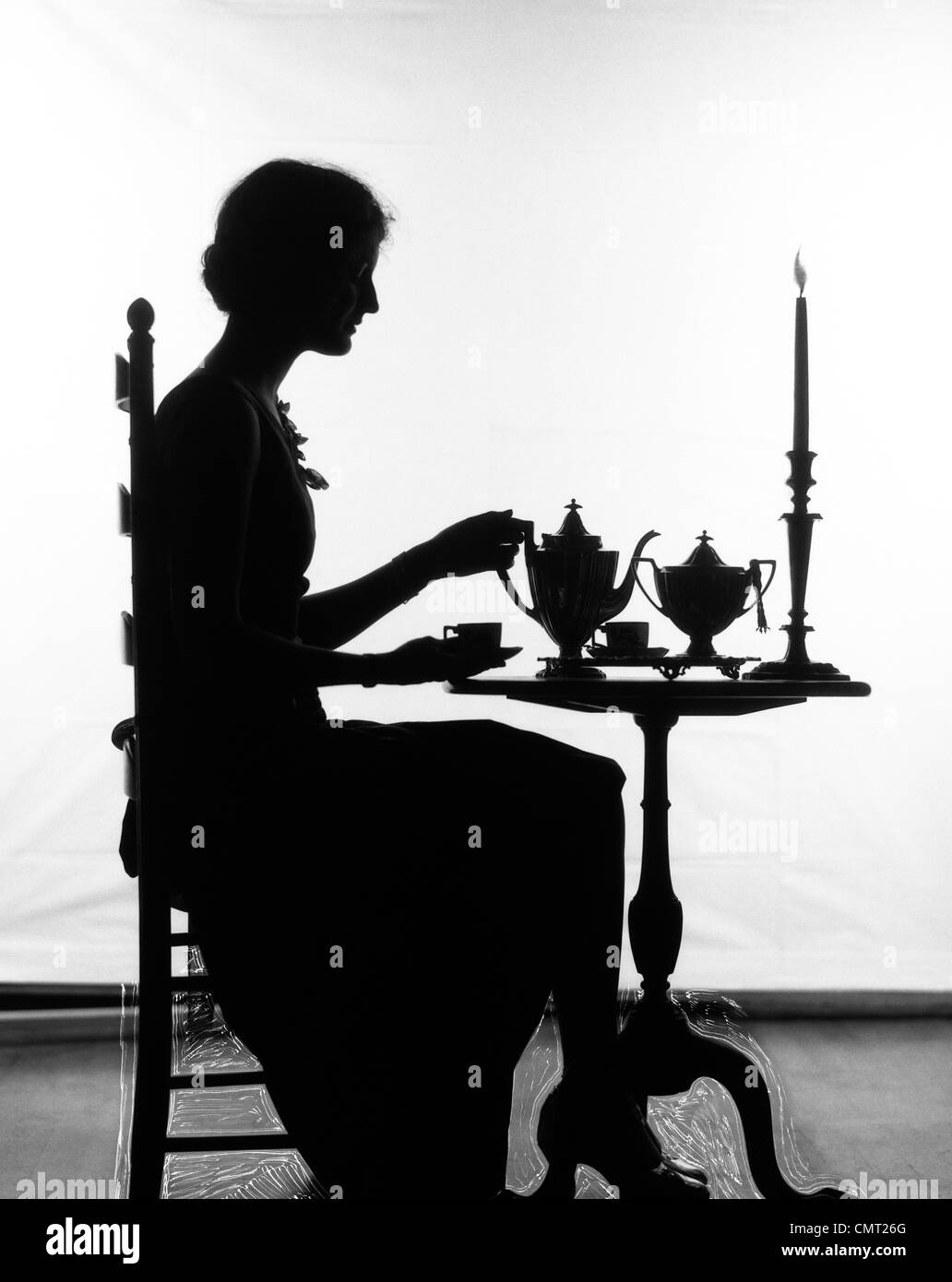 1920ER JAHRE SILHOUETTE DER FRAU SITZT AM TISCH GIEßEN TASSE TEE Stockfoto