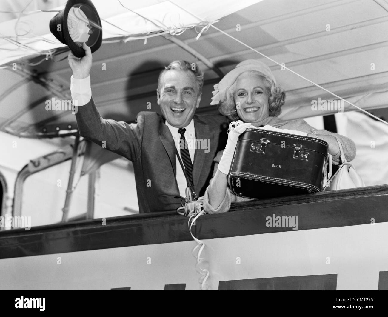 1960ER JAHRE ÄLTERE PAAR MANN UND FRAU LÄCHELND WINKT VON KREUZFAHRTSCHIFF BLICK IN DIE KAMERA Stockfoto