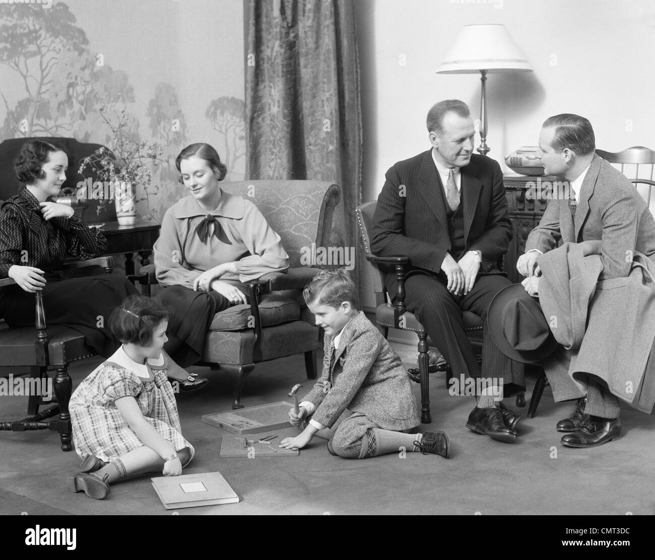 1930ER JAHRE FAMILIE MUTTER VATER ZWEI KINDER SPIELEN ON STOCK BESUCH MIT EINEM ANDEREN PAAR Stockfoto