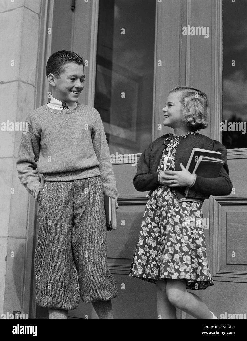 1940ER JAHRE LÄCHELNDE JUNGE & HOLDING MÄDCHENSCHULE BÜCHER VON TÜREN Stockfoto