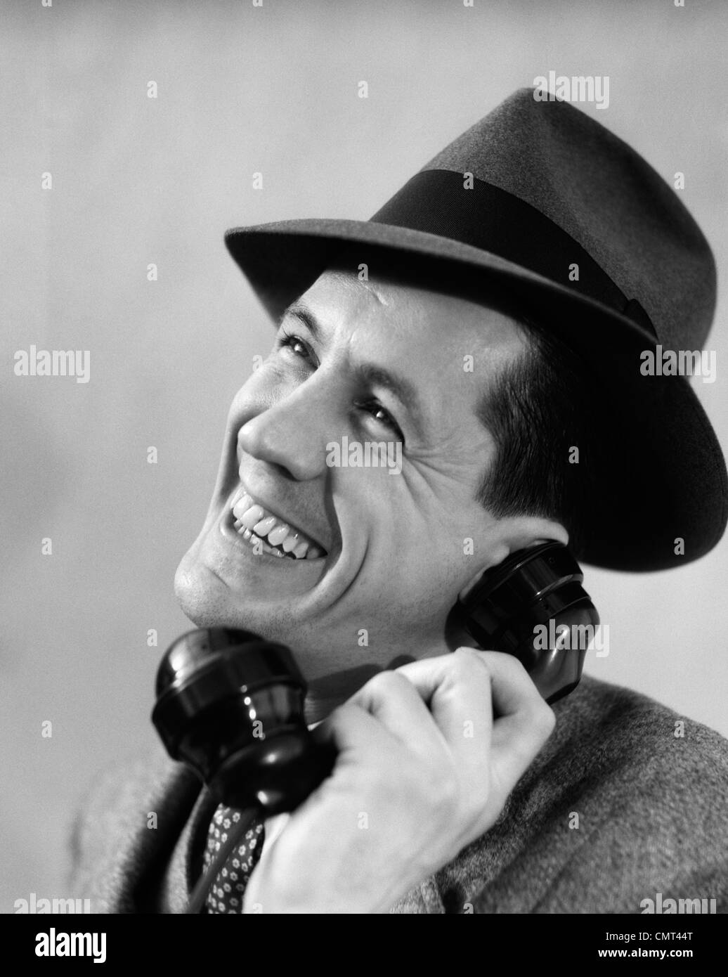 1930ER JAHREN NAHAUFNAHME DER MANN IM ANZUG UND FEDORA HUT LÄCHELND WÄHREND DES GESPRÄCHS AM TELEFON Stockfoto