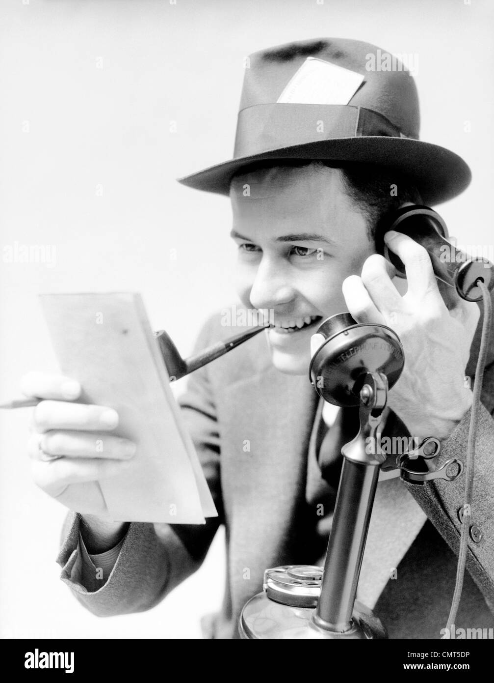 1930ER JAHRE MANN AUFGEREGT ZEITUNG REPORTER RAUCHEN PFEIFE PRESSEAUSWEIS IN HUT TELEFONIEREN AUFRECHT BERICHTERSTATTUNG GESCHICHTE VOM NOTIZBLOCK Stockfoto