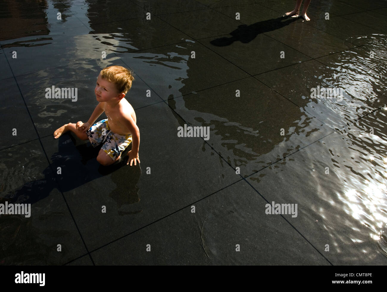 Kleiner Junge sitzt auf dem Boden, umgeben von Pfützen Stockfoto